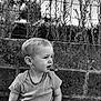 Isaac a rejoint le concours — aidez-le/la à gagner de superbes lots ! toddler, child, boy, portrait, black_and_white, necklace, short_sleeve_shirt, bracelet, stone_wall, wire_fence, plants, outdoor, nature, sitting, expression, curious, texture, casual_clothing, daylight, young