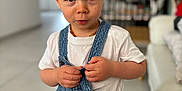 Isaac participe au concours pour gagner de l'argent avec cette photo : baby, blond_hair, casual_clothing, child, closeup, cute, denim_overalls, floor_tiles, furniture, home, indoor, person, portrait, serious_expression, short_hair, sofa, standing, toddler, white_shirt, young_child