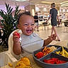 Kylo joined the competition — help win amazing prizes! toddler, high_chair, watermelon, food, croissant, plate, smile, happy, indoor, dining, restaurant, person, curly_hair, bib, table, meal, child, casual_clothing, background_people, modern_interior