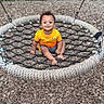toddler, child, swing, rope_swing, playground, orange_shirt, smiling, outdoor, wood_chips, greenery, happy, baby, person, seat, net, summer, fun, cute, park, leisure