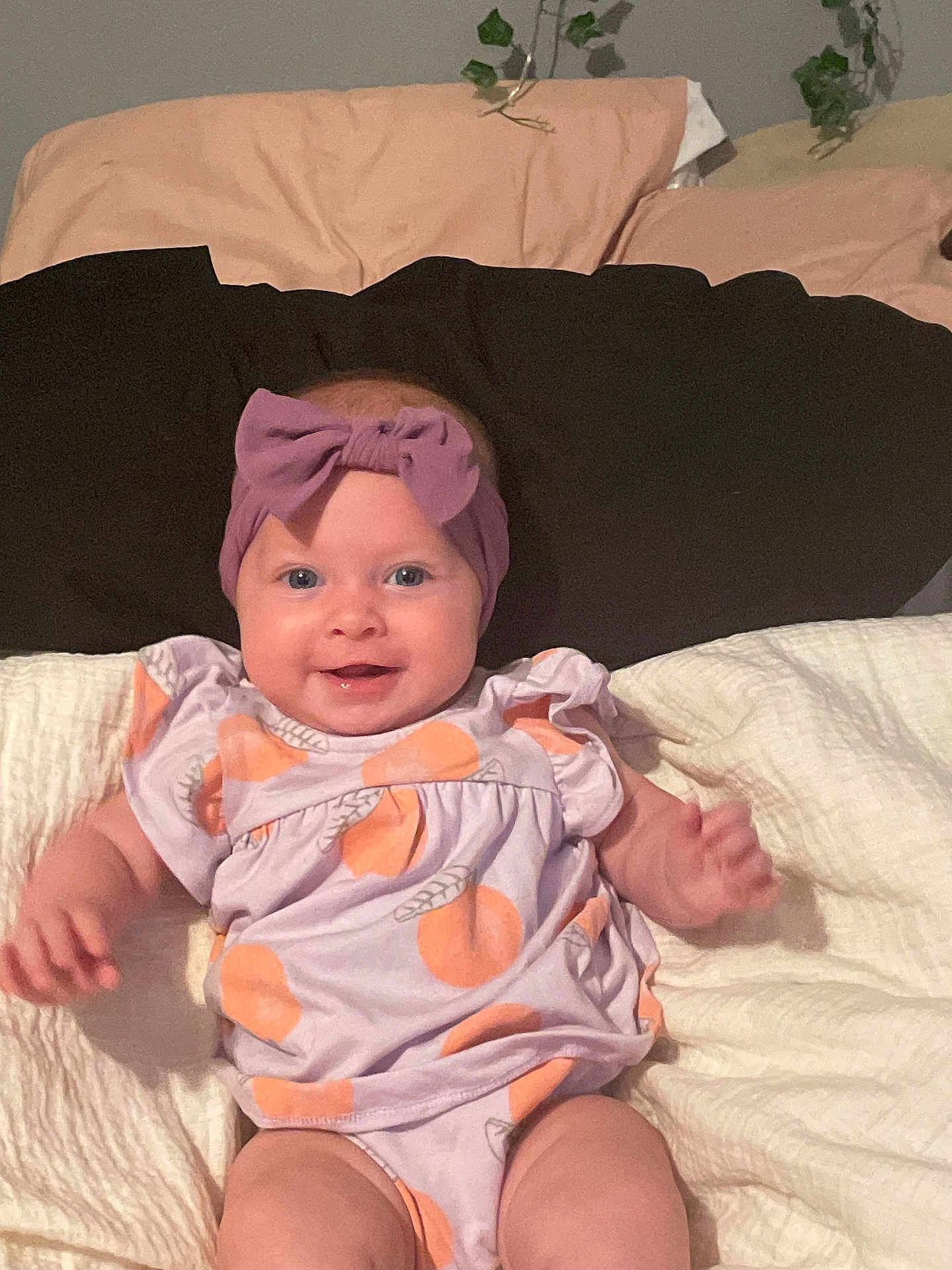 Everley joined the competition — help win amazing prizes! baby, child, smiling, headband, purple_bow, clothing, orange_prints, blanket, bed, pillow, cute, happy, infant, person, portrait, indoors, soft_lighting, skin, face, lying_down