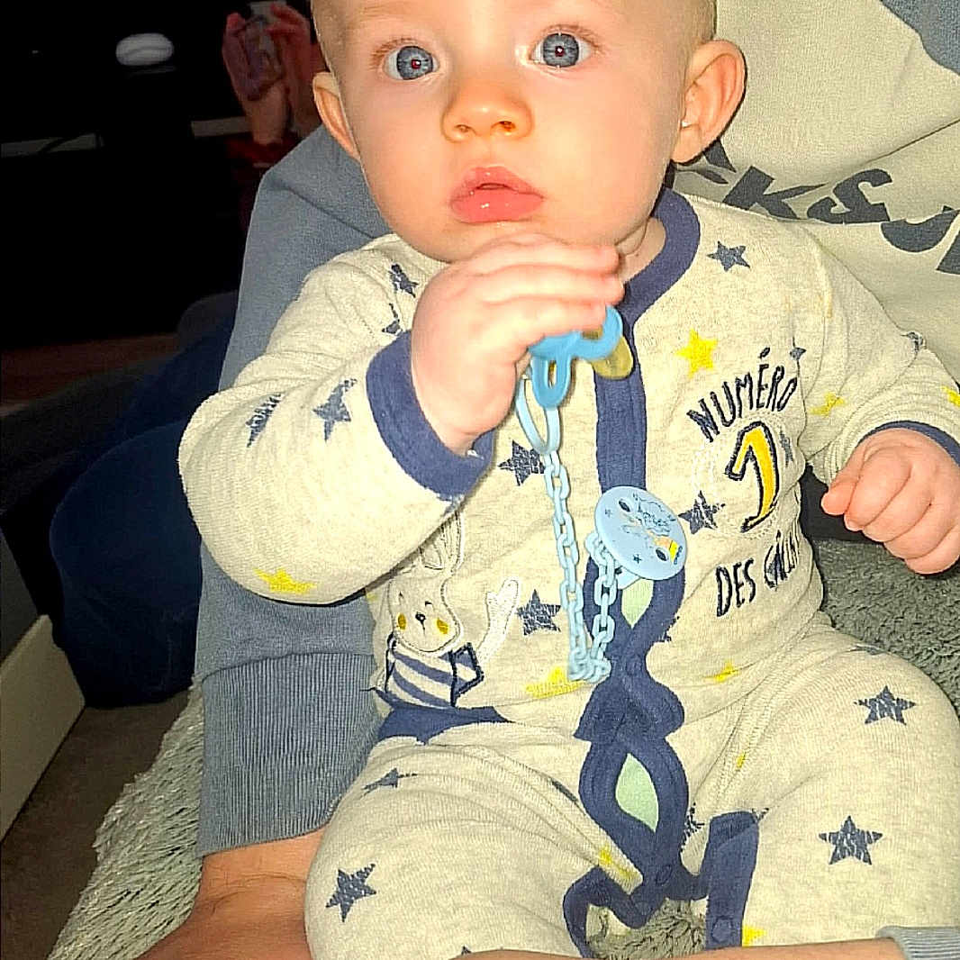 Ayden a rejoint le concours — aidez-le/la à gagner de superbes lots ! adult, baby, blue_eyes, child, closeup, clothing, comfort, cute, furniture, hand, holding, indoor, living_room, pacifier, pajamas, person, portrait, sitting, star_pattern, television
