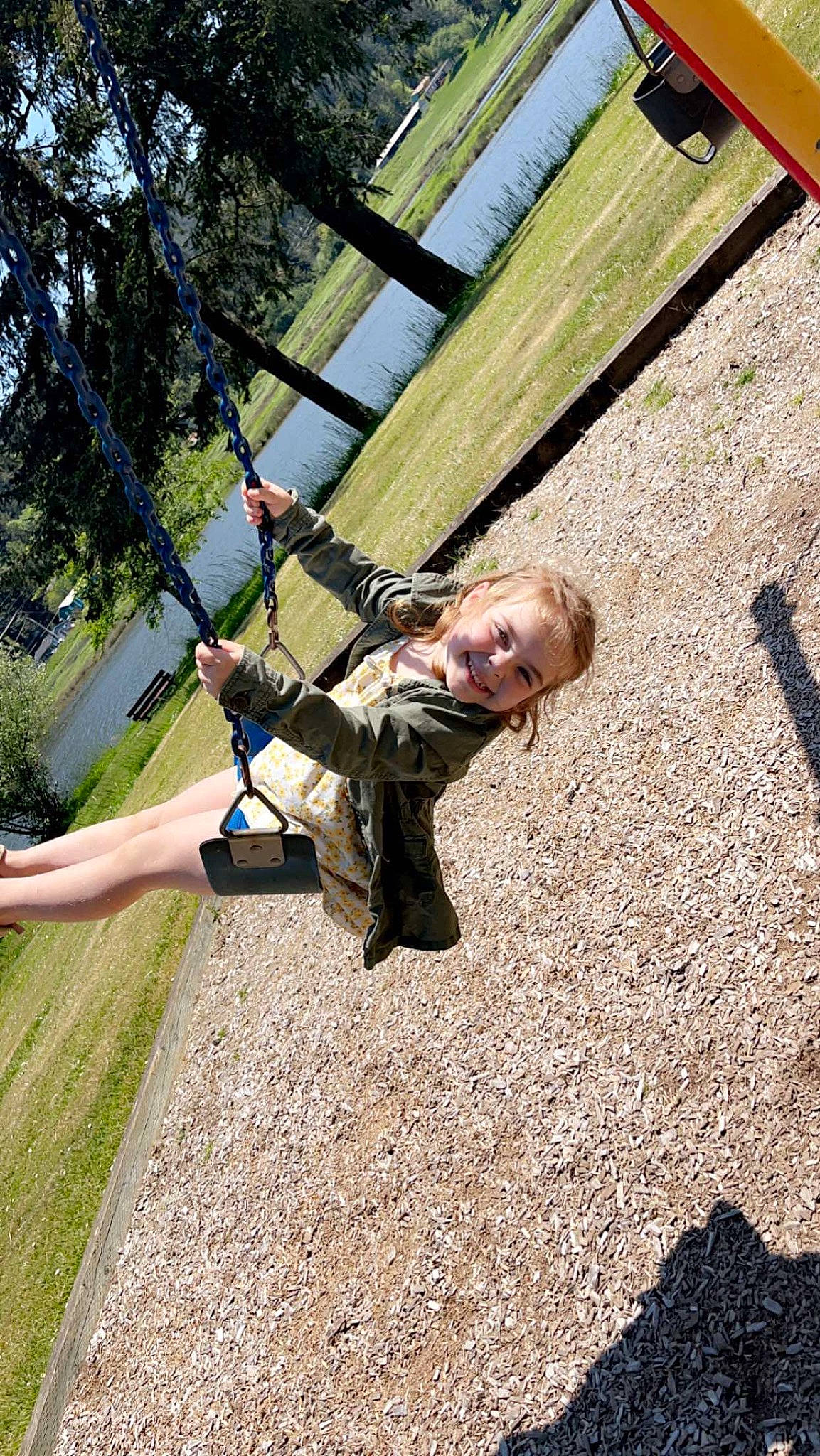 Rylee is registered to the contest to win money with this photo: adventure, city, fun, grass, happy, joy, landscape, leisure, outdoor_play_equipment, people_in_nature, person, plant, playground, recreation, rope, shadow, smile, soil, swing, tree