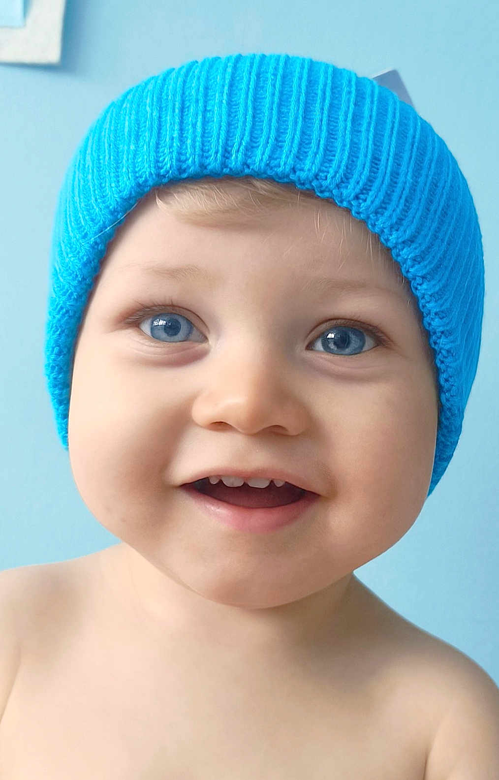 Mayron participe au concours pour gagner de l'argent avec cette photo : baby, child, blue_eyes, smile, hat, knit_hat, portrait, close_up, happy, cute, infant, skin, face, blue_background, headwear, young_child, expression, teeth, cheeks, indoors