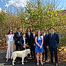 dog, people, group_portrait, outdoor, sunny, blue_sky, trees, garden, formalwear, suits, dresses, friends, family, smiling, standing, leash, cream_dog, pavement, house, daylight