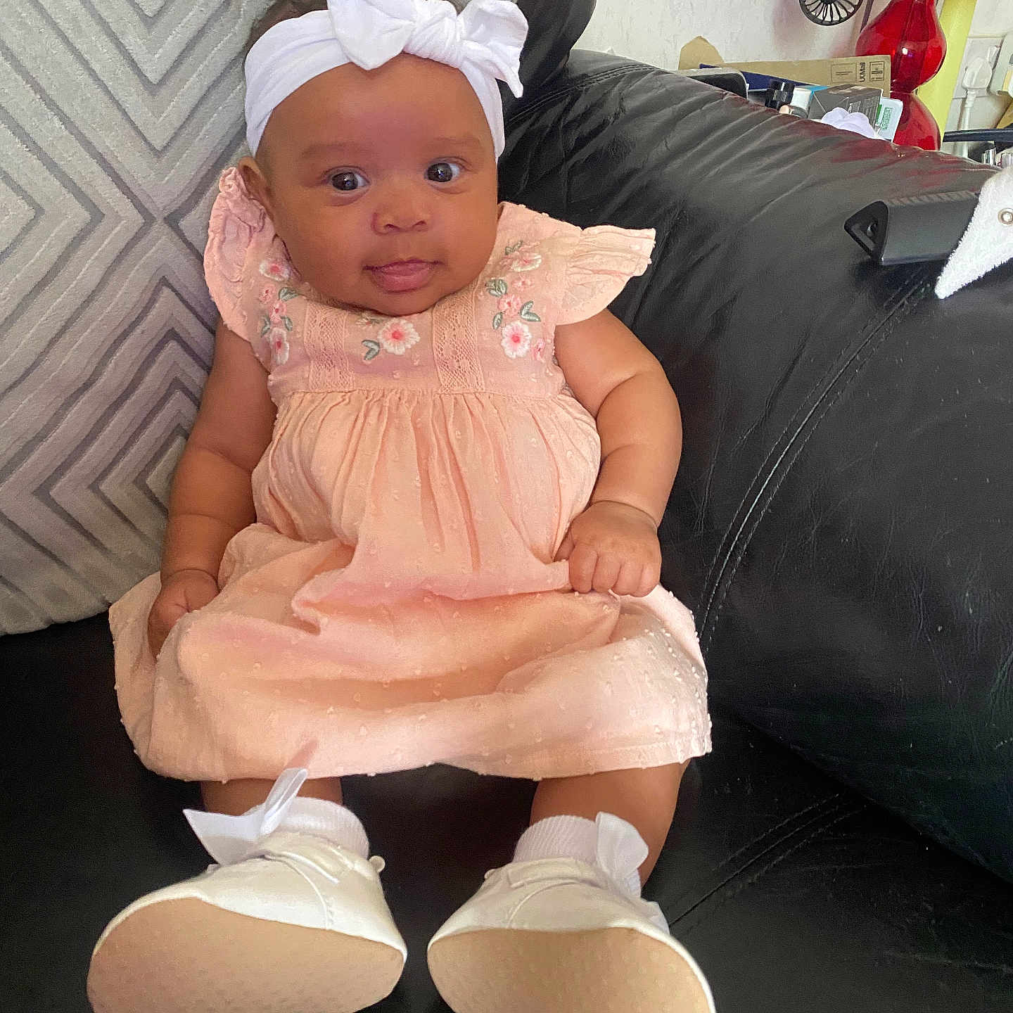 Amara-Mae is registered to the contest to win money with this photo: baby, black_leather, child, couch, curious_expression, cute, dress, girl, headband, home_interior, indoor, infant, lamp, pillow, portrait, red_lamp, seated, shoes, socks, white_bow