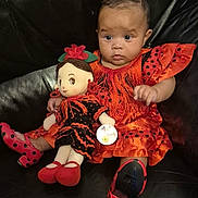 Amara-Mae is registered to the contest to win money with this photo: baby, doll, dress, polka_dot, orange, black_leather, couch, child, toy, footwear, shoes, fringe, sitting, indoor, cute, portrait, expression, fabric, hand, face