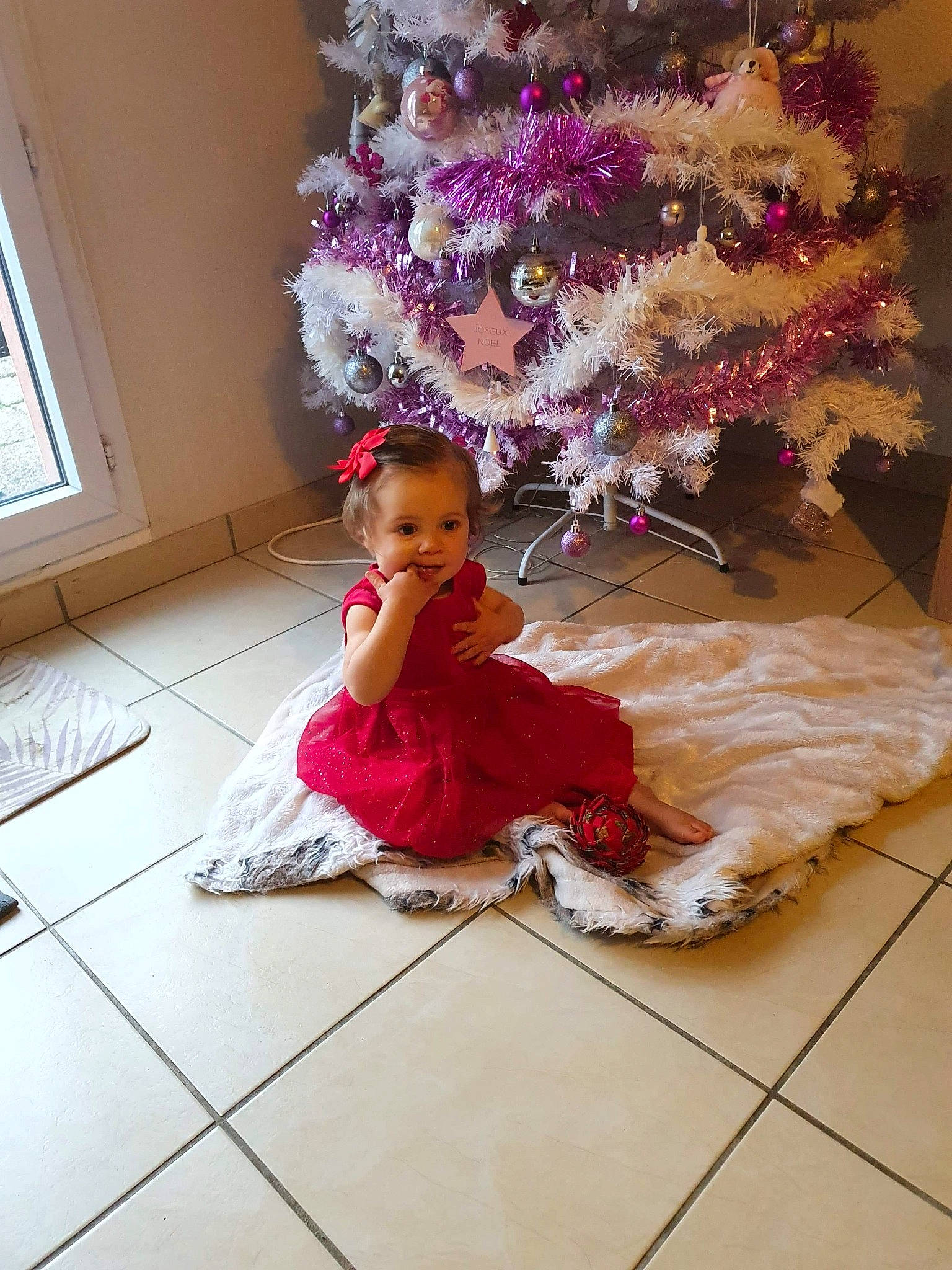 Elyana participe au concours pour gagner de l'argent avec cette photo : baby_toddler_clothing, christmas, christmas_decoration, christmas_eve, christmas_ornament, christmas_tree, dress, floor, flooring, holiday, human, interior_design, magenta, ornament, person, pink, purple, room, toddler, window