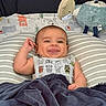 Matthias is registered to the contest to win money with this photo: baby, child, infant, smiling, tongue_out, portrait, lying_down, bed, pillow, blanket, plush_toy, stuffed_animal, nursery, indoors, striped, onesie, toy, happy, cozy, photography