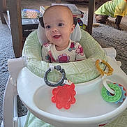 Stormi joined the competition — help win amazing prizes! baby, baby_walker, smiling, toy, indoor, carpet, dog, pet_clothing, wooden_table, books, child, person, green, white, red, yellow, floor, furniture, happy, cute