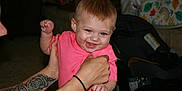 Brianna is registered to the contest to win money with this photo: baby, blue_eyes, car_seat, cheerful, child, clothing, cute, hands, happy, holding, human, indoor, infant, person, pink_shirt, portrait, skin, smiling, tattoo, young_child