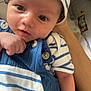 baby, infant, hat, striped_clothing, blue_overalls, buttons, hand, arm, face, eyes, portrait, closeup, smile, skin, fabric, bedding, person, newborn, cute, indoor