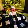 baby, infant, child, christmas_tree, holiday_lights, blanket, plaid, onesie, hat, smile, happy, living_room, bokeh, toy_train, carpet, curtains, sofa, portrait, indoors, decorations