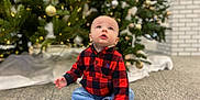 Matt is registered to the contest to win money with this photo: baby, child, infant, christmas_tree, ornament, holiday, indoors, carpet, plaid_shirt, red_plaid, jeans, barefoot, sitting, looking_up, bokeh, lights, pine_tree, cozy, portrait, adorable