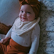 Lilith participe au concours pour gagner de l'argent avec cette photo : baby, child, smile, headband, bow, clothing, pants, onesie, bed, blanket, pattern, floral_pattern, happy, portrait, indoors, infant, cute, cozy, person, resting