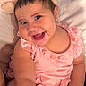 baby, child, infant, smiling, happy, portrait, close_up, pink_outfit, bunny_ears, headband, bed, bedding, indoor, face, eyes, teething, sitting, cozy, adorable, photograph
