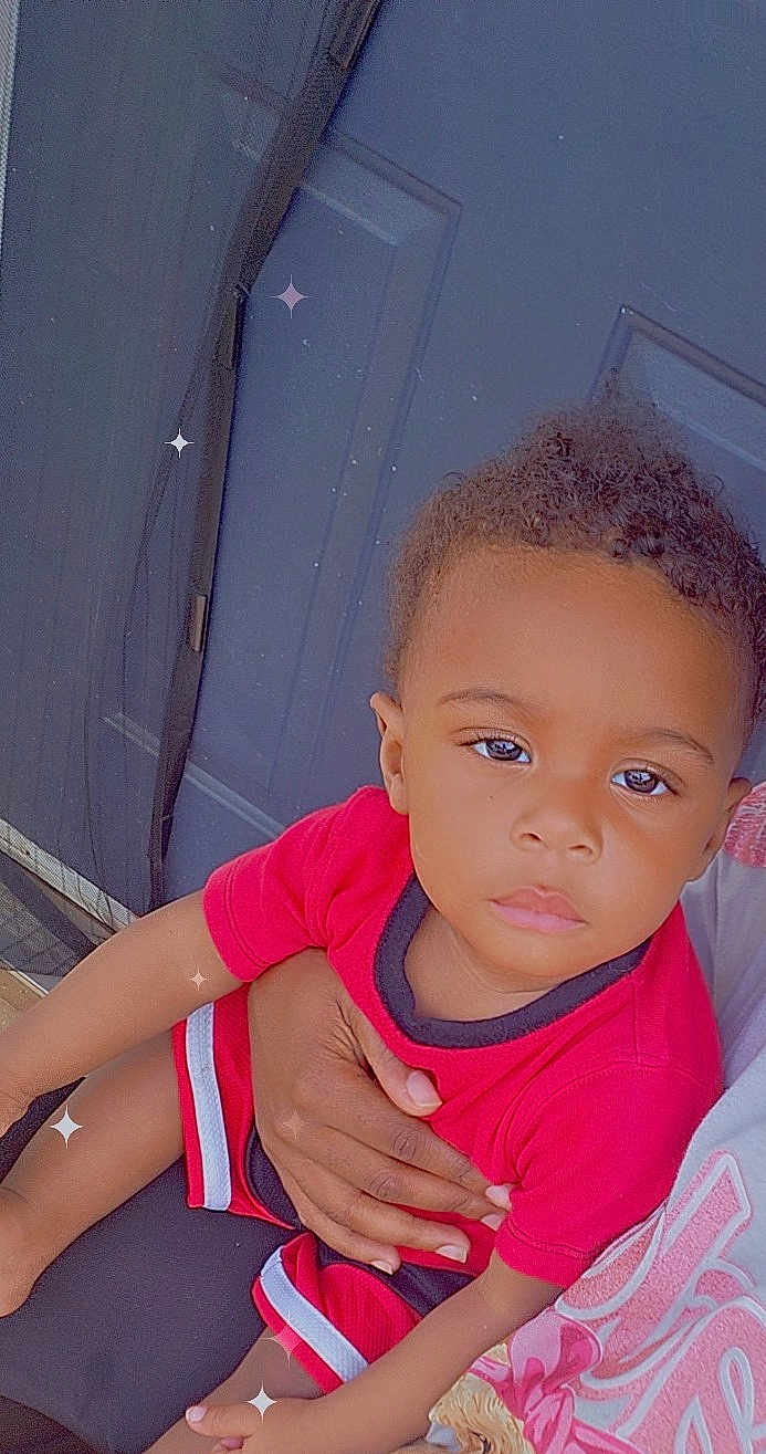 Ty'Zaiah is registered to the contest to win money with this photo: child, toddler, red_clothing, shorts, shirt, hand, adult_hand, door, blue_door, mesh_screen, sparkles, serious_expression, person, indoor, portrait, skin, hair, sitting, closeup, casual