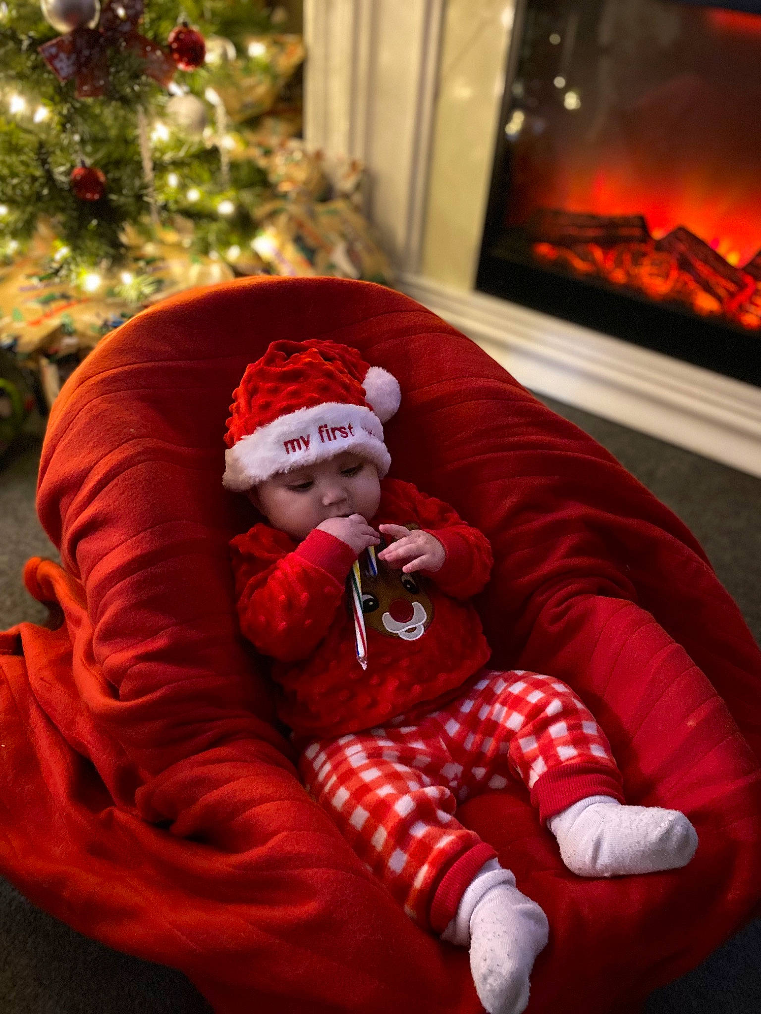 Elliana joined the competition — help win amazing prizes! baby_toddler_clothing, christmas, christmas_decoration, christmas_eve, christmas_ornament, christmas_tree, comfort, event, fire, fireplace, flame, gas, headwear, holiday, lap, person, red, sleeve, snapshot, toddler