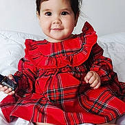 Maria a rejoint le concours — aidez-le/la à gagner de superbes lots ! barefoot, bed, blanket, child, cozy, cute, face, hair_accessory, happy, indoors, person, plaid, portrait, red_dress, sitting, skin, smile, toddler, white_bow, young_child