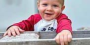 Timéo participe au concours pour gagner de l'argent avec cette photo : child, toddler, smiling, face, hands, wood, fence, red_shirt, blue_eyes, outdoor, portrait, happy, cute, baby, person, wood_texture, plank, casual_clothing, daylight, background_blur