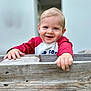 child, toddler, smiling, face, hands, wood, fence, red_shirt, blue_eyes, outdoor, portrait, happy, cute, baby, person, wood_texture, plank, casual_clothing, daylight, background_blur