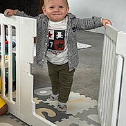 Timéo a rejoint le concours — aidez-le/la à gagner de superbes lots ! toddler, baby_gate, child, smiling, indoor, floor_mat, socks, shirt, pants, kitchen, modern, toy, play_area, person, holding, standing, white, floor, cute, happy
