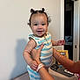 baby, child, smile, curly_hair, striped_clothing, romper, hands, indoor, person, supporting_hands, face, cute, happy, standing, home, wall, picture_frame, remote_control, arm, skin