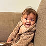 Isabella is registered to the contest to win money with this photo: baby, child, smiling, robe, brown, couch, indoor, face, person, happy, seated, soft, cozy, furniture, hands, portrait, cute, young, expression, warm