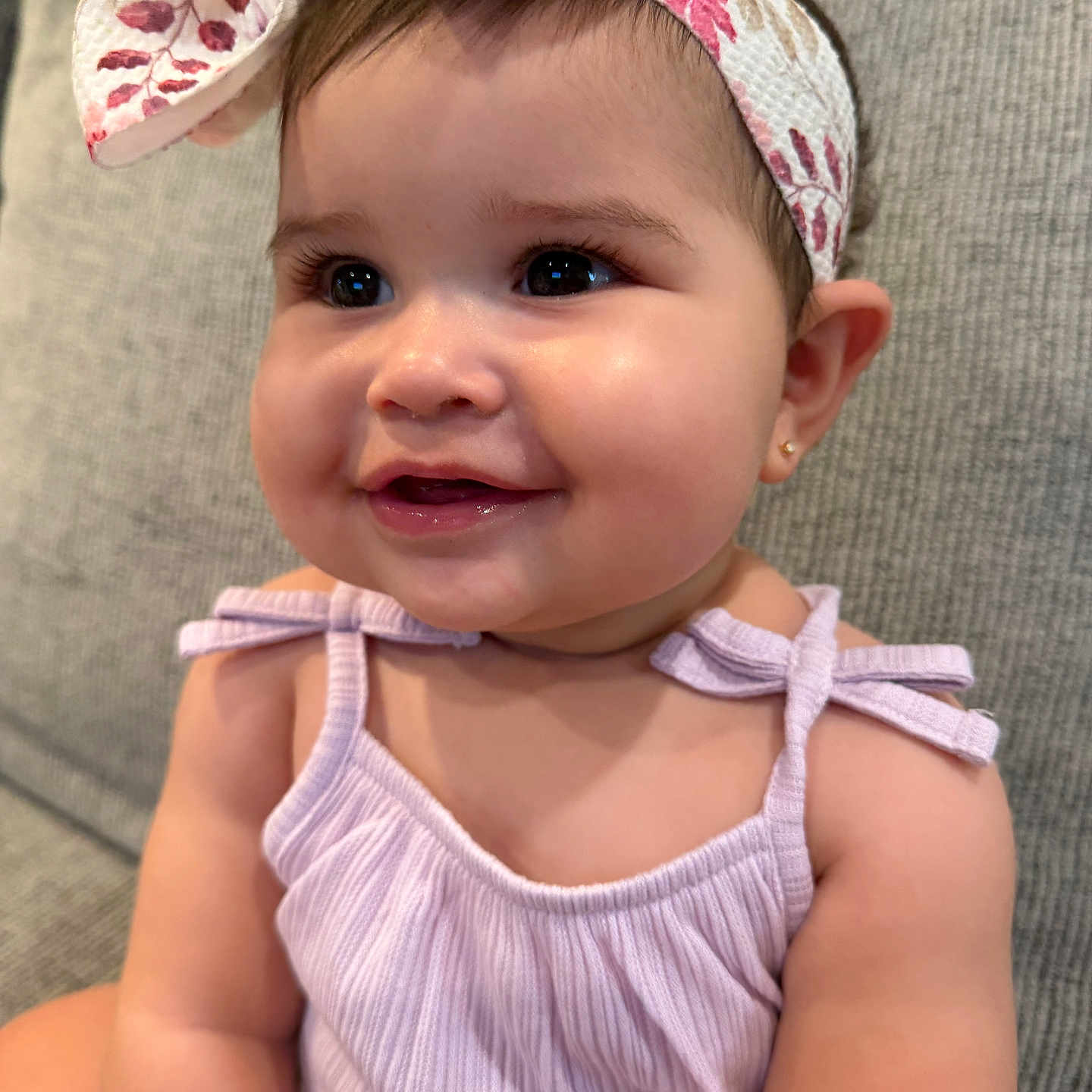 Stori joined the competition — help win amazing prizes! baby, child, girl, smile, face, headband, clothing, purple_dress, earrings, couch, furniture, indoors, skin, cute, happy, portrait, infant, head, person, closeup