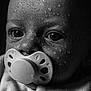 baby, close_up, black_and_white, pacifier, water_droplets, portrait, infant, face, skin_texture, expression, monochrome, wet, newborn, cute, child, eyes, nose, mouth, clothing, soft_light