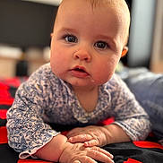 Enora a rejoint le concours — aidez-le/la à gagner de superbes lots ! baby, blanket, blue_eyes, child, close_up, curious, drool, expression, face, hands, head, indoors, infant, lying_down, patterned_clothing, person, portrait, skin, soft_light, young