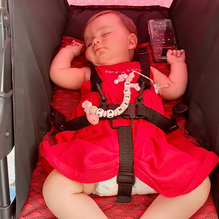 Candice participe au concours pour gagner de l'argent avec cette photo : baby, baby_products, baby_toddler_clothing, car_seat, comfort, finger, happy, human_leg, knee, lap, magenta, pattern, person, pink, red, skin, sleeve, thigh, thumb, toddler