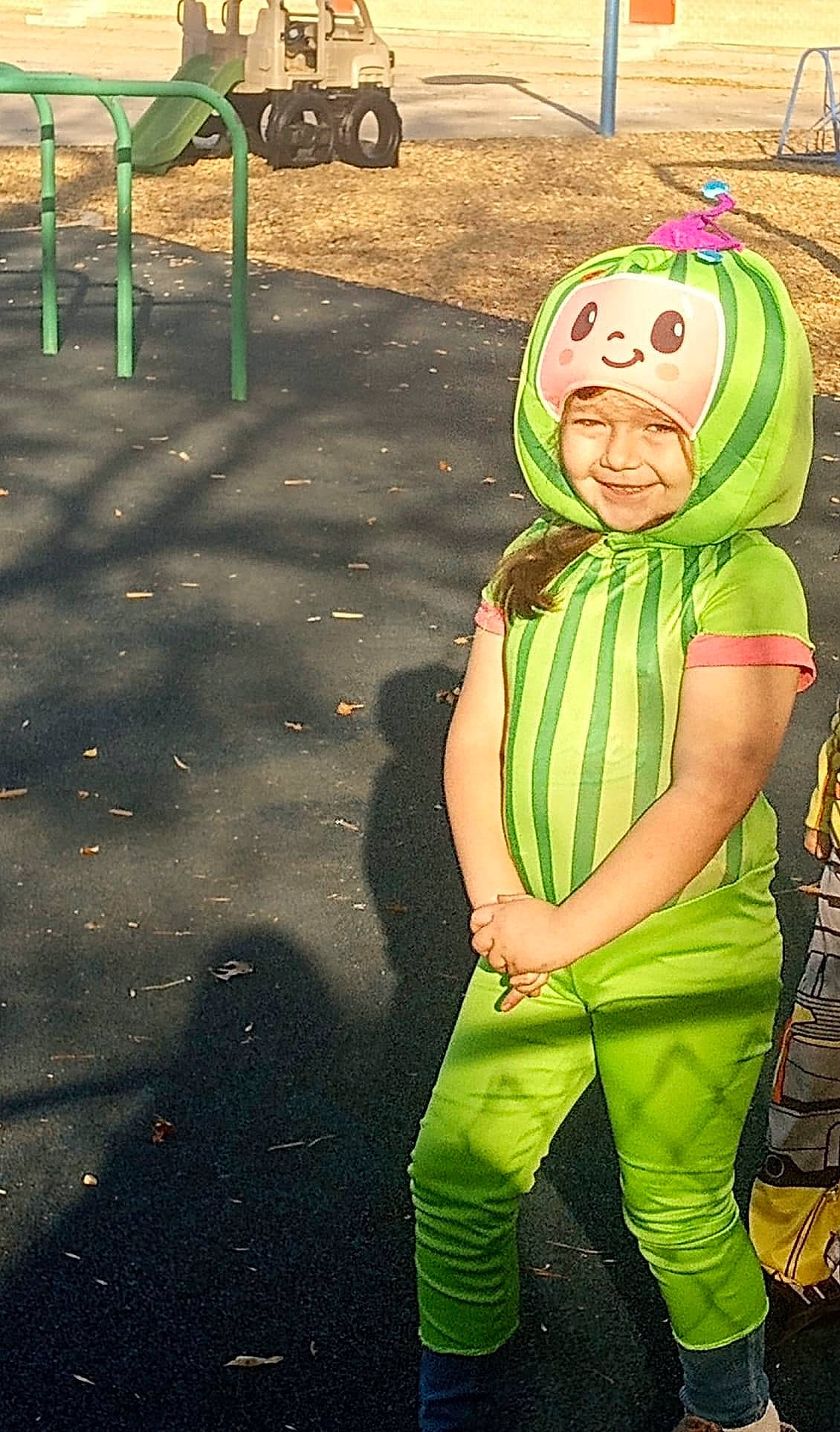 Alice is registered to the contest to win money with this photo: calabaza, child, costume, fictional_character, fun, glove, grass, green, happy, headwear, joy, leisure, mask, people_in_nature, person, personal_protective_equipment, pumpkin, scarf, shadow, soil