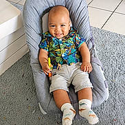 Maël a rejoint le concours — aidez-le/la à gagner de superbes lots ! baby, baby_seat, carpet, child, clothing, colorful, cute, floor_tiles, happy, home, indoor, infant, person, playful, portrait, shirt, smiling, socks, toy, tropical