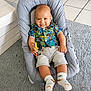 Maël a rejoint le concours — aidez-le/la à gagner de superbes lots ! baby, baby_seat, carpet, child, clothing, colorful, cute, floor_tiles, happy, home, indoor, infant, person, playful, portrait, shirt, smiling, socks, toy, tropical