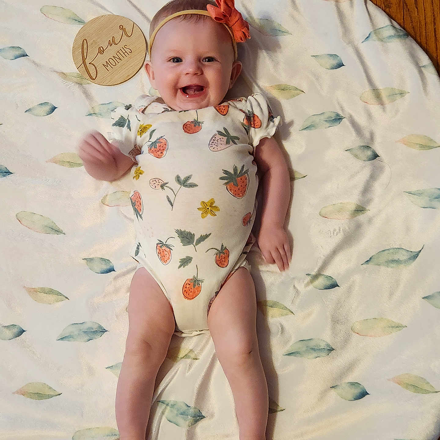 Ember is registered to the contest to win money with this photo: arms, baby, blanket, child, cute, floor, flower, four_months, happy, headband, indoor, infant, leaf_pattern, legs, lying_down, onesie, person, skin, smiling, wooden_marker