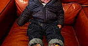 Levi is registered to the contest to win money with this photo: beanie, brown, casual, child, clothing, couch, cute, footwear, indoor, jacket, leather, pants, person, portrait, shoes, sitting, sneakers, toddler, warm_clothing, young_child