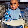 baby, child, high_chair, bib, pajamas, indoor, kitchen, fan, utensils, plate, face, person, cute, infant, tableware, cabinet, countertop, expression, sitting, clothing