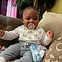 Levi is registered to the contest to win money with this photo: baby, pacifier, bib, striped_shirt, couch, cushion, toy, indoor, child, infant, sitting, clothing, person, home, furniture, smiling, cute, face, young, relaxing