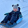 child, toddler, sled, snow, winter_clothing, hat, gloves, outdoor, play, happy, smile, cold_weather, recreation, snow_sledding, winter_fun, blue_sled, snow_tracks, young_child, park, active