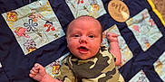 Theodore joined the competition — help win amazing prizes! baby, infant, child, quilt, carpet, camouflage_shirt, black_pants, lying_down, smiling, happy, cute, indoor, colorful, cartoon_characters, fabric, pattern, person, portrait, young, playful