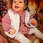 Louison participe au concours pour gagner de l'argent avec cette photo : baby, child, smile, red_checkered_clothing, white_vest, tights, golden_shoes, blanket, christmas_tree, ornaments, fireplace, fire, teddy_bear, holiday, indoors, festive, warm_lighting, cute, portrait, happy