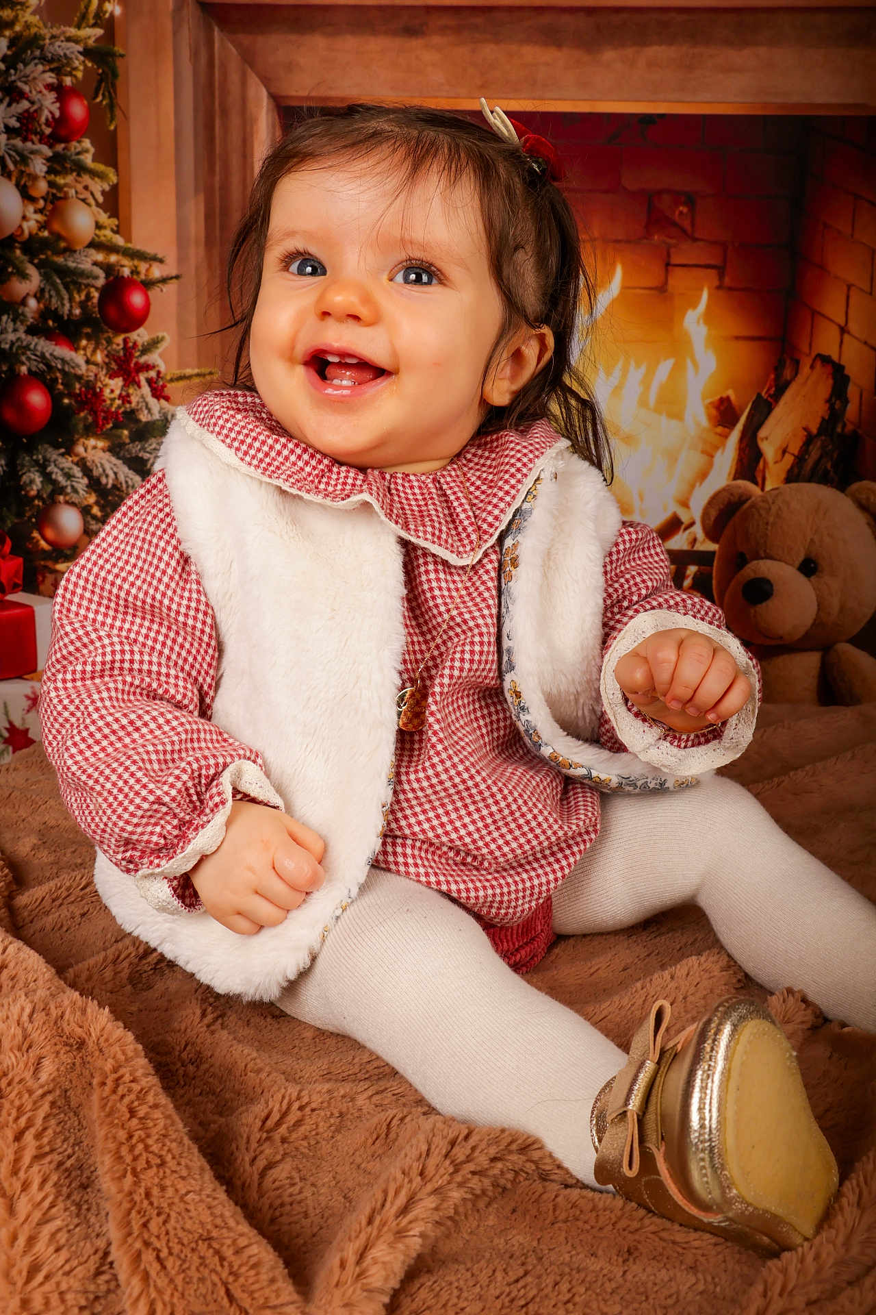 Louison participe au concours pour gagner de l'argent avec cette photo : baby, child, smile, red_checkered_clothing, white_vest, tights, golden_shoes, blanket, christmas_tree, ornaments, fireplace, fire, teddy_bear, holiday, indoors, festive, warm_lighting, cute, portrait, happy