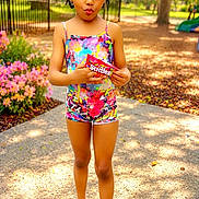 Zeezee joined the competition — help win amazing prizes! child, girl, colorful_clothing, outdoor, park, pathway, flowers, trees, daylight, skittles, holding, footwear, sandals, playful_expression, standing, nature, greenery, sunlight, pavement, summer
