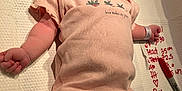 Mable is registered to the contest to win money with this photo: newborn, baby, infant, onesie, hat, wristband, ankleband, hospital, marker, notes, lying_down, face, skin, person, clothing, bed, textile, comfort, peaceful, cute