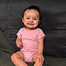 Luna is registered to the contest to win money with this photo: baby, child, pink_onesie, smiling, sitting, couch, fabric, texture, indoor, person, face, happy, infant, young_child, home, furniture, portrait, cute, skin, arm