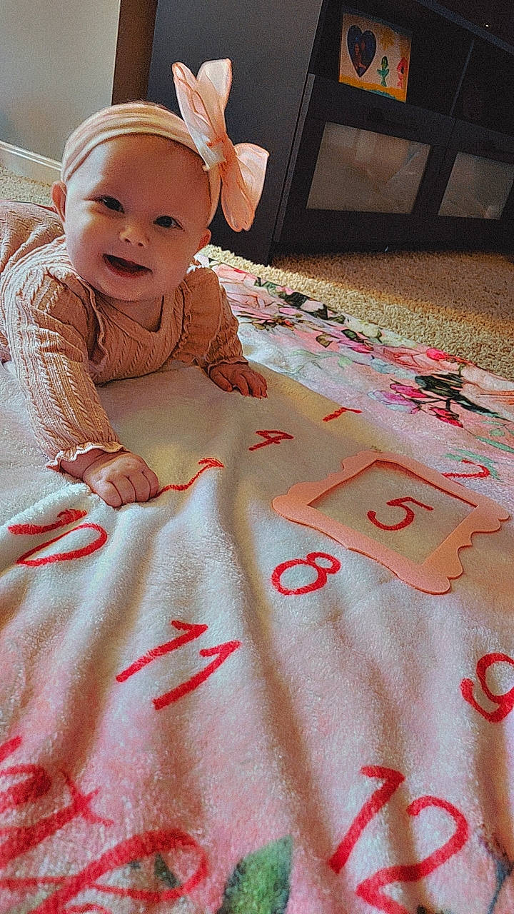 Ava is registered to the contest to win money with this photo: applique, baby, bed, bedroom, blanket, crawling, crib, face, furniture, head, indoors, infantbed, pattern, person, photography, portrait, quilt, room, sitting, text
