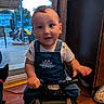 toddler, child, denim_overall, dinosaur, toy_vehicle, indoor, home, wooden_floor, glass_door, backyard, furniture, curtain, footwear, person, baby, face, hand, play, smile, motion_blur