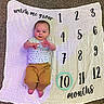 Jackson is registered to the contest to win money with this photo: baby, infant, milestone_blanket, numbers, months, smiling, lying_down, carpet, clothing, white_shirt, mustard_pants, child, young_child, cute, happy, indoors, portrait, hands, feet, growth