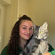 Théodore a rejoint le concours — aidez-le/la à gagner de superbes lots ! woman, cat, pet, curly_hair, green_sweater, indoor, portrait, smile, holding, gray_tabby, sunlight, yellow_eyes, face, feline, happy, human, long_hair, animal, cozy, casual